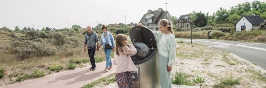 2 kinderen droppen afval correct in de afvalcontainer - de grootouders kijken er blij naar
